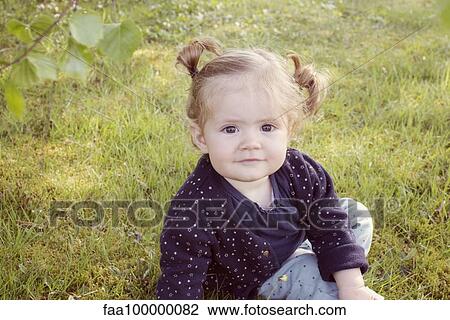 Stock Image - Baby girl sitting on grass, portrait. Fotosearch