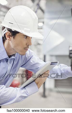 Engineer referencing digital tablet while working inside industrial plant View Large Photo Image Stock Image - Engineer referencing digital tablet while working inside industrial plant. Fotosearch