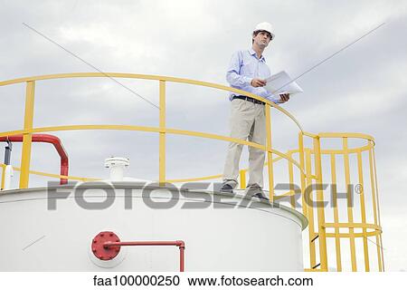 Stock Image - Engineer reviewing plans at industrial plant. Fotosearch