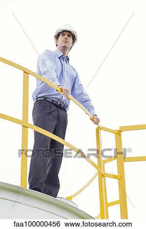 Engineer standing on top of storage tank at industrial plant View Large Photo Image Stock Photograph - Engineer standing on top of storage tank at industrial plant. Fotosearch