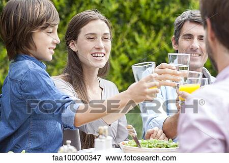 Stock Photo - Family clinking glasses at outdoor gathering. Fotosearch