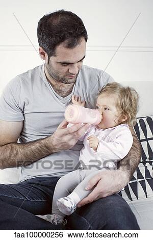 Stock Photograph - Father holding baby girl on lap, feeding her with bottle. Fotosearch
