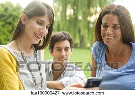 Stock Photo - Friends looking at smartphone outdoors. Fotosearch