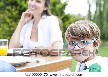 Little boy sitting at outdoor table with family, smiling at camera View Large Photo Image Stock Image - Little boy sitting at outdoor table with family, smiling at camera. Fotosearch