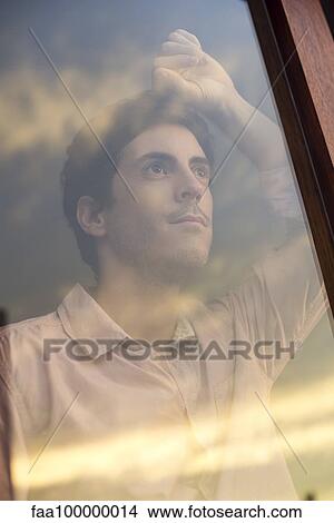 Picture - Man looking out hotel window at sunset. Fotosearch