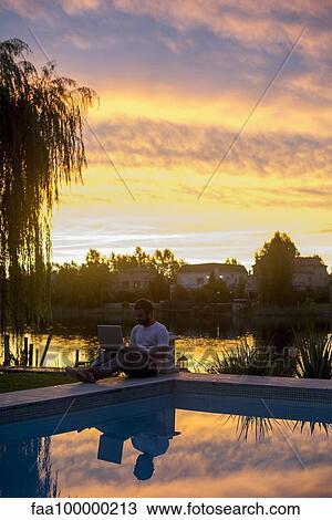 Man sitting next to pool using laptop computer View Large Photo Image Stock Image - Man sitting next to pool using laptop computer. Fotosearch