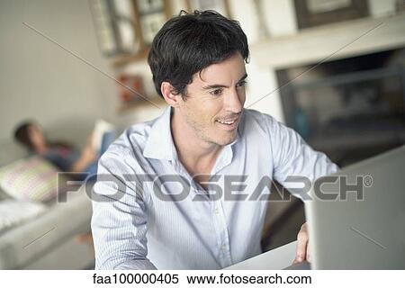 Stock Photography - Man using laptop computer in living room. Fotosearch