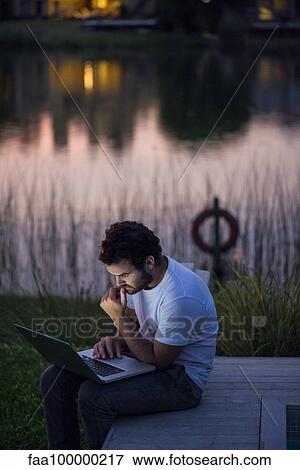 Man using laptop computer on lakeshore deck View Large Photo Image Stock Photo - Man using laptop computer on lakeshore deck. Fotosearch
