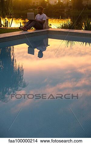 Man using laptop next to hotel swimming pool View Large Photo Image Picture - Man using laptop next to hotel swimming pool. Fotosearch