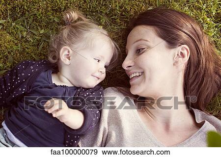 Stock Photo - Mother and baby girl lying on grass, smiling at each other. Fotosearch