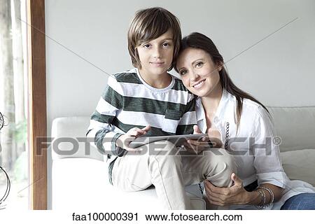 Mother and son sitting together on sofa with digital tablet View Large Photo Image Stock Image - Mother and son sitting together on sofa with digital tablet. Fotosearch
