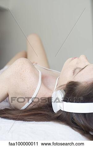 Stock Image - Reclining woman listening to music on headphones. Fotosearch
