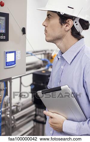 Stock Image - Technician checking industrial equipment in operation at plant. Fotosearch