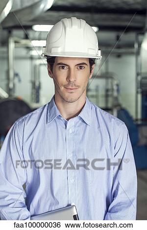 Stock Photograph - Technician inside industrial plant, portrait. Fotosearch