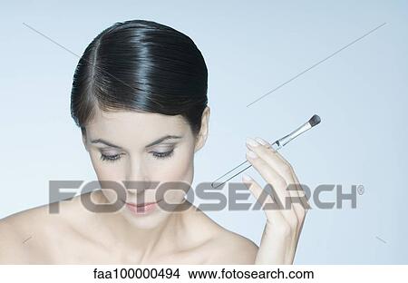 Woman holding eye shadow brush, looking down View Large Photo Image Picture - Woman holding eye shadow brush, looking down. Fotosearch