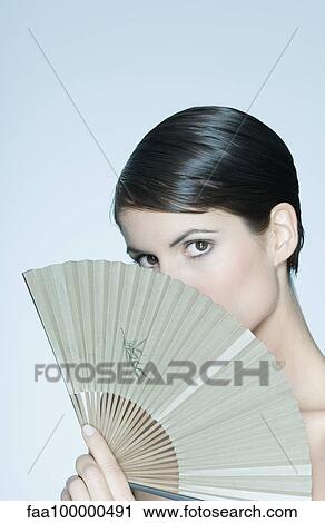 Woman holding fan in front of her face, portrait View Large Photo Image Stock Image - Woman holding fan in front of her face, portrait. Fotosearch