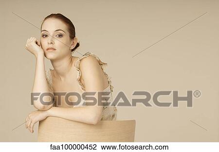 Stock Image - Woman leaning against back of chair, portrait. Fotosearch