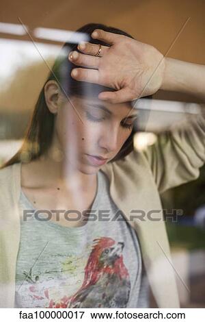 Stock Photo - Woman leaning against window looking down with air of disappointment. Fotosearch