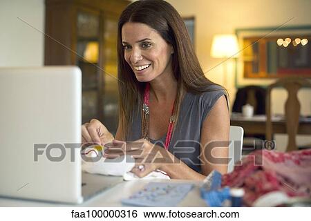 Woman looking at laptop computer while sewing View Large Photo Image Stock Photograph - Woman looking at laptop computer while sewing. Fotosearch