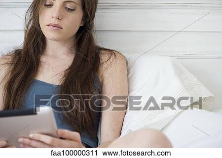 Woman sitting in bed using digital tablet View Large Photo Image Stock Image - Woman sitting in bed using digital tablet. Fotosearch