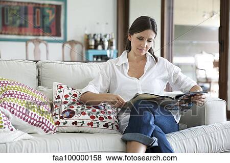 Woman sitting on sofa reading magazine View Large Photo Image Stock Photo - Woman sitting on sofa reading magazine. Fotosearch
