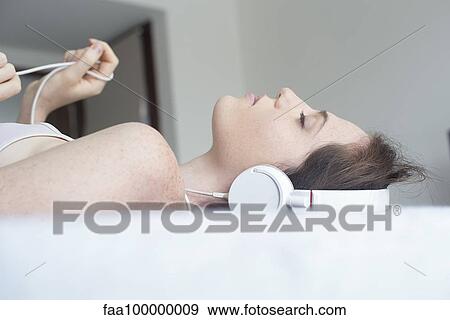 Stock Photo - Woman wearing headphones lying down. Fotosearch