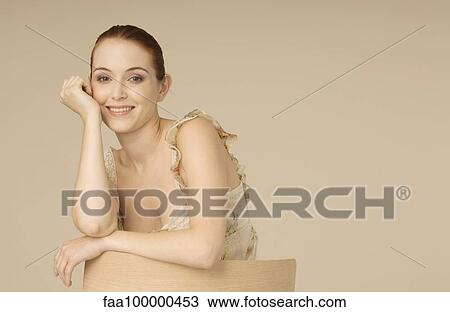 Stock Image - Young woman leaning against back of chair, portrait. Fotosearch