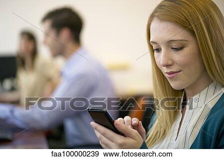 Stock Photo - Young woman using smartphone in office. Fotosearch