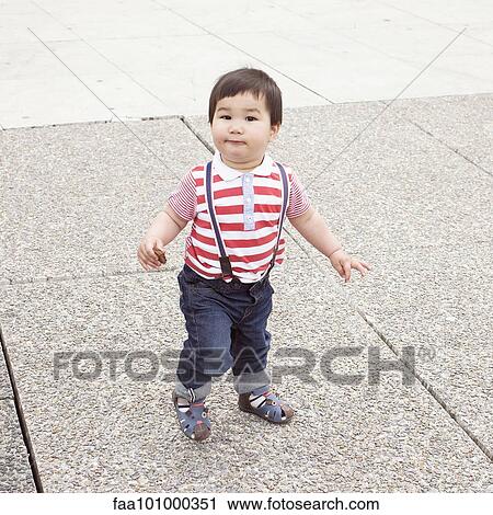 Stock Image - Baby boy walking on sidewalk with snack in hand. Fotosearch