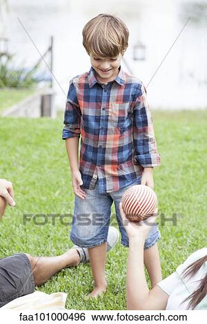 Boy playing ball at lakeside park with family View Large Photo Image Stock Photograph - Boy playing ball at lakeside park with family. Fotosearch