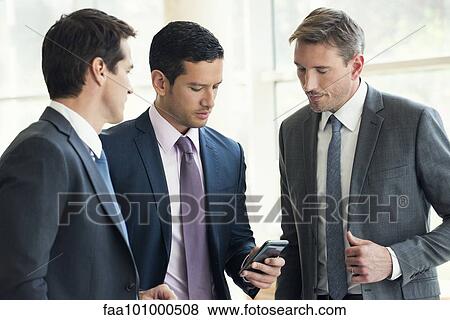 "Businessman talking with colleagues, looking at smartphone" View Large Photo Image Stock Photo - "Businessman talking with colleagues, looking at smartphone". Fotosearch