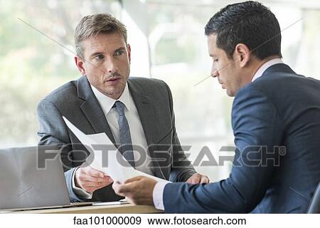 Stock Photo - Businessmen discussing documents in meeting. Fotosearch
