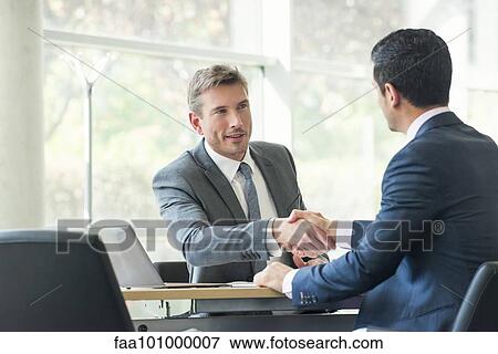Stock Photo - Businessmen shaking hands in meeting. Fotosearch