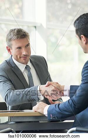 Stock Photograph - Businessmen shaking hands in meeting. Fotosearch