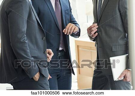 Stock Photograph - Businessmen standing chatting before meeting. Fotosearch