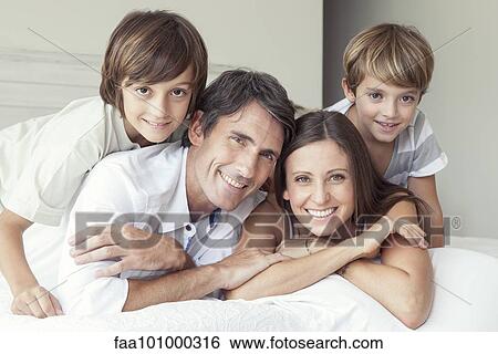 Stock Photograph - "Family lying on bed, portrait". Fotosearch
