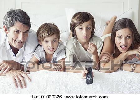 Stock Photograph - "Family watching TV on bed, portrait". Fotosearch