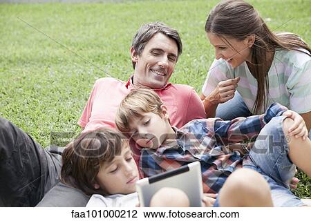 "Family with two children spending afternoon at park, young boys using digital tablet" View Large Photo Image Stock Image - "Family with two children spending afternoon at park, young boys using digital tablet". Fotosearch