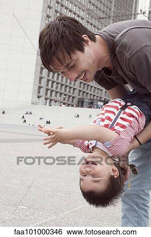 Stock Photograph - "Father holding young son upside down, both laughing". Fotosearch