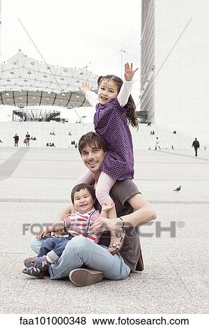 Stock Photo - Father sitting on the ground with two children in city square. Fotosearch