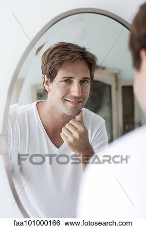 Man looking at self in mirror touching facial stubble View Large Photo Image Stock Photograph - Man looking at self in mirror touching facial stubble. Fotosearch