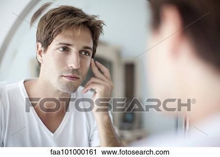Stock Image - Man looking at self in mirror with concern about his complexion. Fotosearch