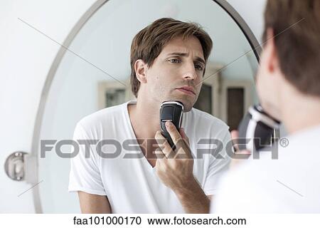 Stock Image - Man shaving with electric razor. Fotosearch