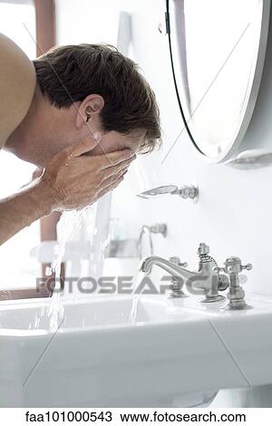Stock Image - Man washing face in bathroom sink. Fotosearch