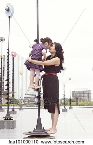 Stock Image - Mother and daughter nuzzling while standing on whimsical sculpture. Fotosearch