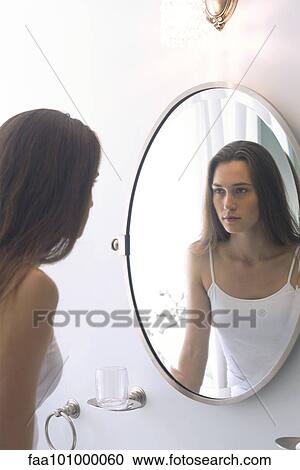 Stock Image - Woman looking at self in bathroom mirror. Fotosearch