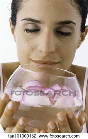 Stock Image - Woman smelling petals floating in bowel of water. Fotosearch