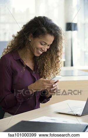 Woman text messaging with smartphone in office View Large Photo Image Stock Photo - Woman text messaging with smartphone in office. Fotosearch