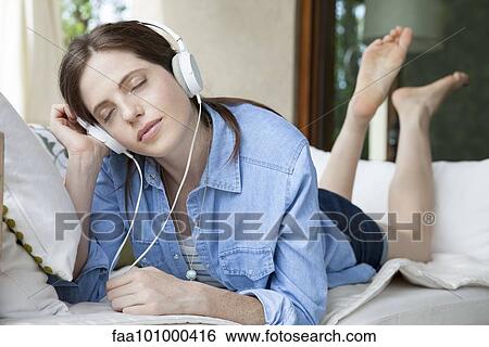 "Young woma lying on stomach, listening to headphones with eyes closed" View Large Photo Image Stock Photograph - "Young woma lying on stomach, listening to headphones with eyes closed". Fotosearch