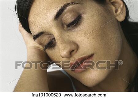 Stock Image - "Young woman holding head, looking down, portrait". Fotosearch